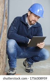 tradesman crouching and looking at a tablet