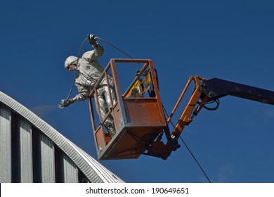 Tradesman Spray Painting The Roof Of An Industrial Building