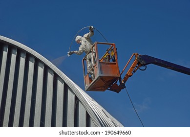 Tradesman Spray Painting The Roof Of An Industrial Building