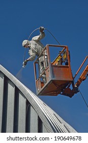 Tradesman Spray Painting The Roof Of An Industrial Building