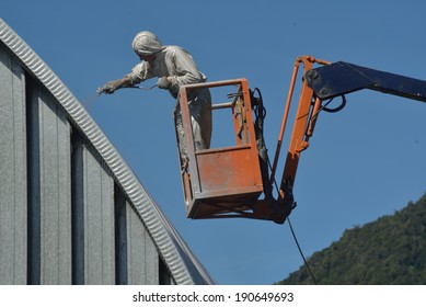 Tradesman Spray Painting The Roof Of An Industrial Building