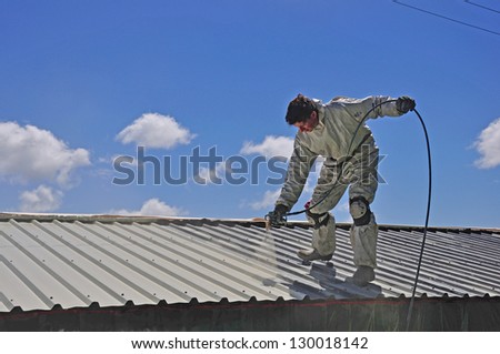 A tradesman uses an airless spray to paint the roof of a building