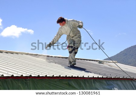 A tradesman uses an airless spray to paint the roof of a building