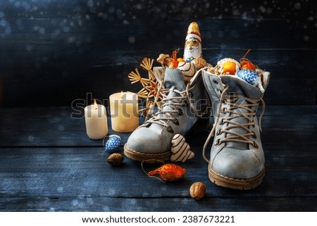Tradition on German Nikolaus Tag meaning Nicholas day, shoes are filled with treats, here boots with sweets and Christmas decoration on dark blue wood with candles, copy space, selected focus