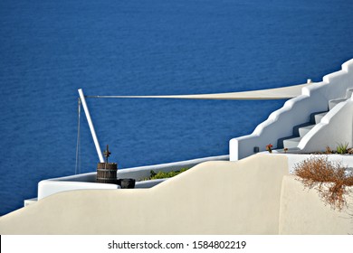 Traditional Adobe House With A Sun Shade Sail And Slate Steps Overlooking The Aegean Sea In Santorini Island, Cyclades Greece. 