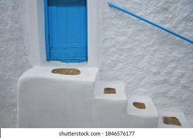 Traditional Adobe House With A Whitewashed Wall, Stone Steps And A Light Blue Wooden Door With Matching Railing In Amorgos Island, Cyclades Greece. 