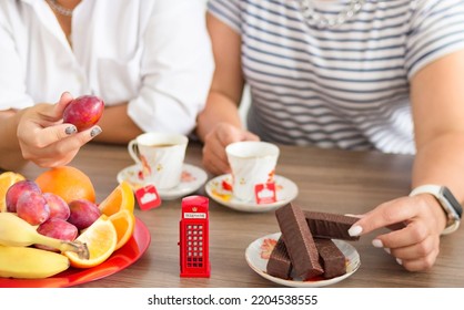 Traditional Afternoon Tea Of British Ceremony With Such Symbol Of Britishness As Toy Telephone Box, Defocused Faceless Women On Background, Front Focus