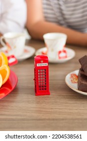 Traditional Afternoon Tea Of British Ceremony With Such Symbol Of Britishness As Toy Telephone Box, Defocused Faceless Women On Background, Front Focus, Vertical Image