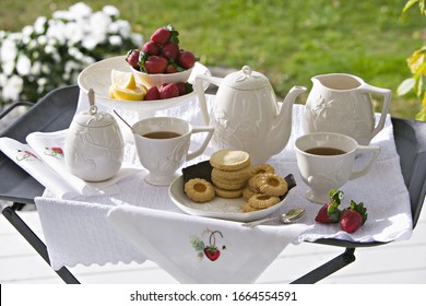 A traditional afternoon tea set out on a tea tray in a garden with white china and strawberries. - Powered by Shutterstock