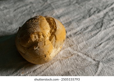 A traditional Alentejano paposeco bread sits on a white tablecloth, capturing the simplicity of Portuguese cuisine. The rustic bread contrasts beautifully with the clean, white setting. - Powered by Shutterstock