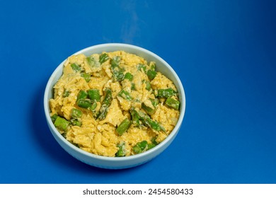 A traditional Alentejo dish, featuring scrambled eggs mixed with vibrant green asparagus. The golden hues of the eggs contrast beautifully with the deep blue background. - Powered by Shutterstock