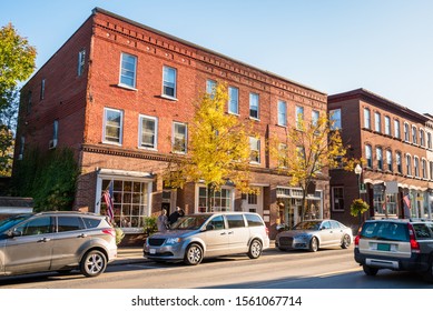 Traditional American brick buildings with shops along a busy street at sunset. Woodstock, VT, USA.