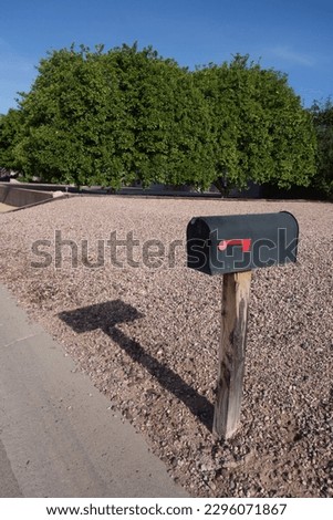 Traditional American roadside metal mailbox painted in black with red drop flag on a weathered wooden post
