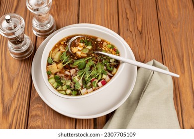 Traditional ancient Russian okroshka soup with turkey meat, vegetables and kvass on a wooden table. Summer refreshing hearty dish.