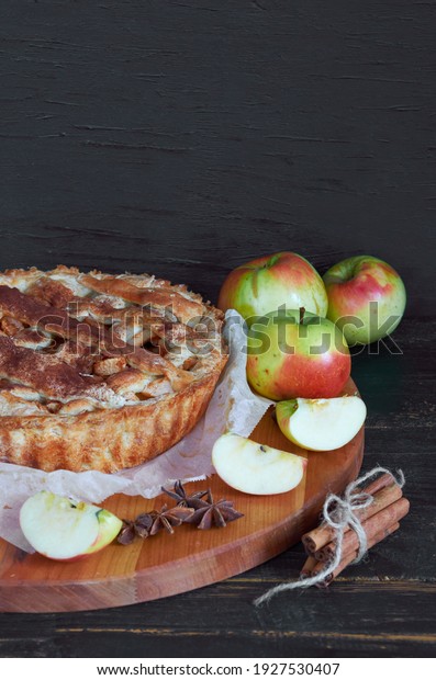 Traditional apple\
pie with spices on the brown wooden board. Apple pie decorated with\
sliced fresh apples and cinnamon sticks on the black background.\
Side view  with copy\
space