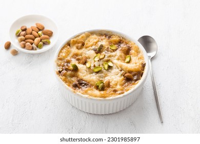 Traditional Arabic dessert Umm Ali in a white ceramic form decorated with nuts on a light gray background