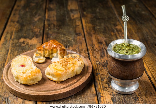 Traditional Argentinian yerba mate tea in a\
calabash gourd with bombilla stick and argentine pastries desserts\
against wooden\
background