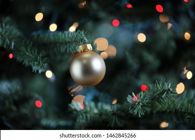 Traditional artificial Christmas tree with gold ball ornament and glowing colorful lights in background 