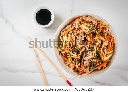 Traditional Asian food. Lunch stirfry: rice noodles, zucchini, carrots, bamboo, mushrooms, pork (beef), soy sauce and black sesame. With soy sauce, chopsticks. Copy space top view