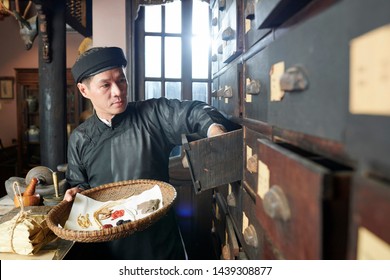 Traditional Asian Herbal Medicine Practitioner Opening Drawers And Filling Bowl With Ingredients For Treatment