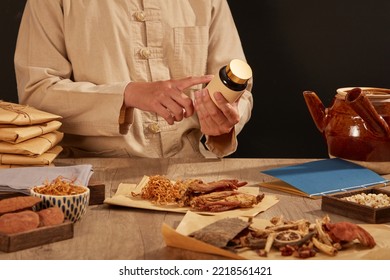 Traditional Asian Herbal Medicine Practitioner Checking Medicine With A Table Covered In Raw Ingredients Medicine.