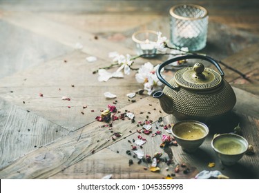 Traditional Asian tea ceremony arrangement. Iron teapot, cups, dried rose buds and candles over wooden table background, selective focus, copy space