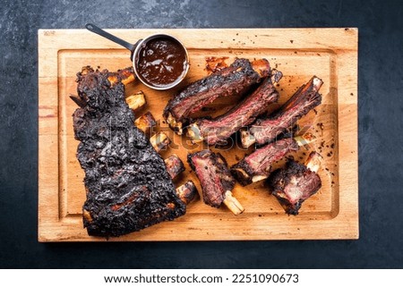 Traditional Barbecue burnt beef ribs St Louis style sliced and offered as top view on a rustic wooden board 
