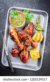 Traditional barbecue chicken drumsticks with corn and chimichurri sauce as top view in a silber fryer 