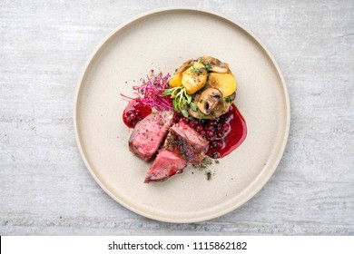 Traditional barbecue dry aged sliced venison fillet steak with potato mushroom terrine and cowberry sauce as top view on a plate with copy space