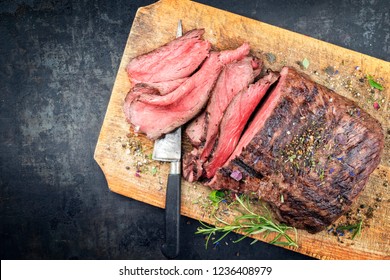 Traditional barbecue dry aged sliced roast beef steak with herbs as top view on an old cutting board with copy space left