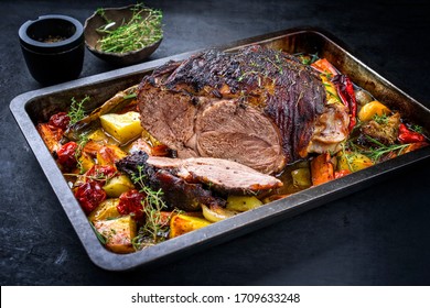 Traditional barbecue lamb roast sliced with tomatoes and fried potatoes as closeup in a metal tray 