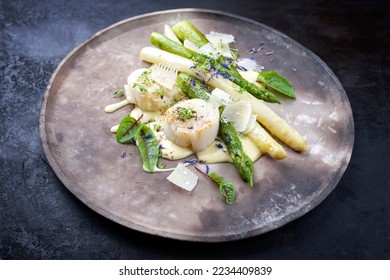Traditional barbecue scallops with green and white asparagus and sauce hollandaise offered as close-up on a rustic modern design plate 