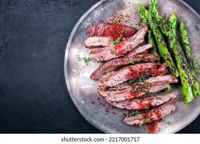 Traditional Barbecue Sliced Dry Aged Wagyu Flank Steak Offered With Green Asparagus And Chili Powder Offered As Overhead View On A Rustic Modern Design Plate With Copy Space Left 