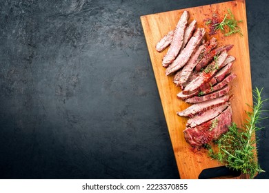 Traditional Barbecue Sliced Dry Aged Wagyu Flank Steak Offered With Herbs And Chili Powder As Overhead View On A Modern Design Wooden Board With Copy Space Left 