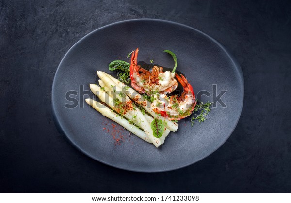 Traditional barbecue spiny lobster tail sliced and\
offered with white asparagus and lettuce as top view on a modern\
design plate 