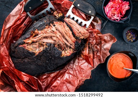 Traditional barbecue wagyu pulled beef in peach paper with Carolina BBQ sauce and onion rings as top view on a rustic board