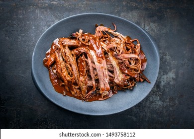Traditional barbecue wagyu torn to bits pulled beef in hot chili sauce in a modern design cast iron plate as top view on a rustic board with copy space 