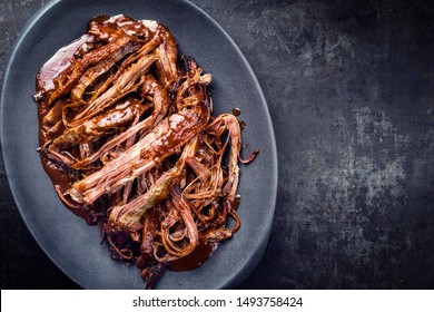 Traditional barbecue wagyu torn to bits pulled beef in hot chili sauce in a modern design cast iron plate as top view on a rustic board with copy space right