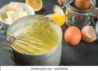 Traditional Basic Sauces. French Cuisine. Hollandaise Sauce In A Metal Saucepan, With Ingredients For Cooking - Eggs, Butter, Lemons. On A Black Stone Table. Copy Space Top View