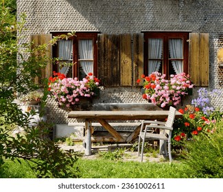 a traditional Bavarian country house covered with wood shingles with lush geraniums on the window ledge in the Bavarian Alps on a warm day in September, Oberjoch, Bad Hindelang, Bavaria, Germany      