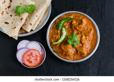 Traditional Bengali Masala Chicken Curry with gravy and Chapati hot and spicy dish on black background Kolkata, India. side dish Murgir Jhol served with Roti, rice, naan, Paratha or Parantha.