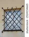 Traditional black wrought iron window grill on a pale yellow stucco wall. The ornate metalwork features scroll designs, providing security and aesthetic appeal to the building’s exterior architecture