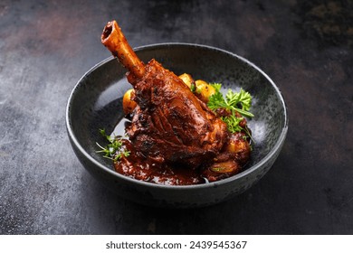 Traditional braised slow cooked lamb knuckle in red wine sauce with mini roast potatoes and herbs served as close-up in a Nordic design bowl with copy space - Powered by Shutterstock