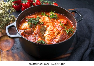 Traditional Brazilian fish stew moqueca baiana with fish filet in tomato sauce as closeup in a modern design cast-iron roasting dish 