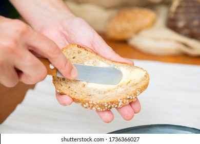 Traditional breakfast cooking. Hands of woman spreading butter onto slice of baguette with knife over table with bread and napkin. Closeup shot. Bread or eating concept