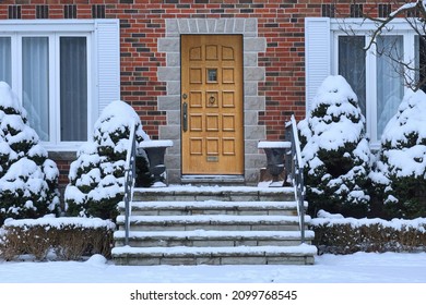 Traditional Brick House With Wood Grain Front Door And Snow Covered Shrubbery