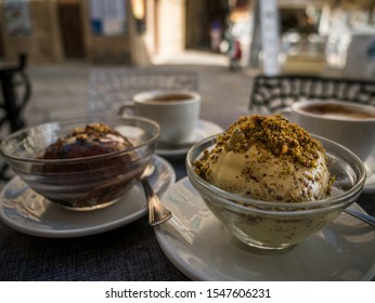 Traditional Calabrian Tartufo ice cream in cross-section with nougat filling at a cafe in Pizzo, chcocolate nougat and pistachio ice cream balls and cappuccino cups on a table infront of a cafe 