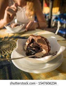 Traditional Calabrian Tartufo ice cream in cross-section with nougat filling at a cafe in Pizzo, woman sitting and eating a dessert in the background