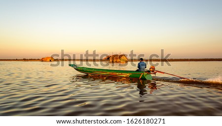 Traditional Cambodian Long Boat Passing in Front of Bamboo Thatch Hut on the Shore where the Mekong River Meets Tonle Sap Lake Near Siem Reap  Cambodia 