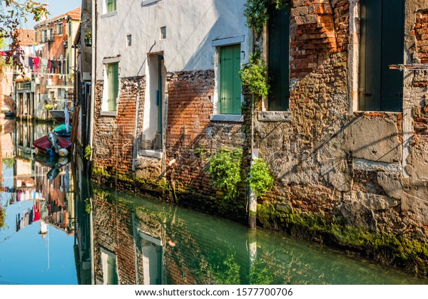 Traditional canal street\
with reflection in the water laundry hanging out of a typical\
Venetian facade.\
Italy.